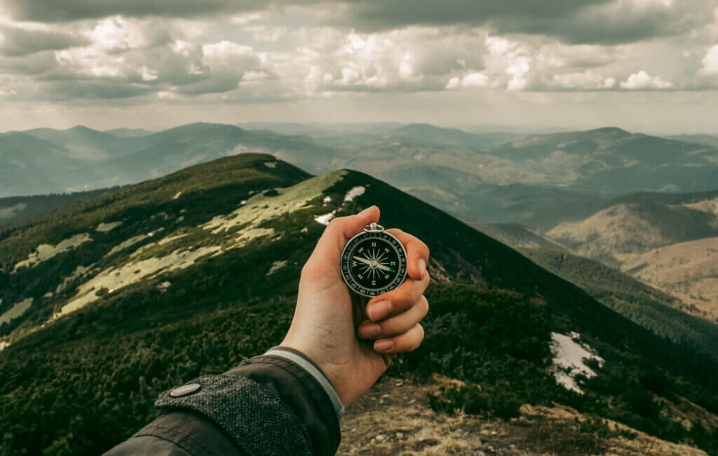 picture of a hand holding a compass on top of a mountain