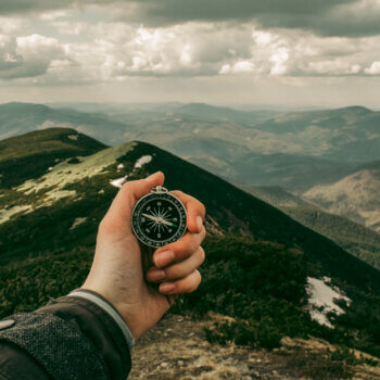 picture of a hand holding a compass on top of a mountain
