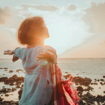 picture of woman with outstretched arms looking towards the sun