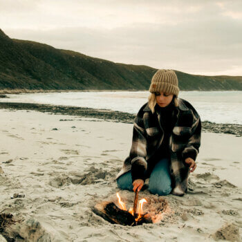 woman building a fire on a deserted beach