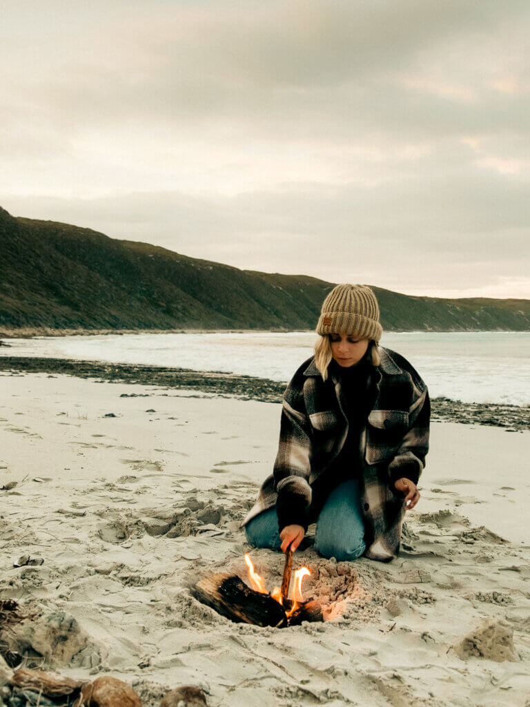 woman building a fire on a deserted beach