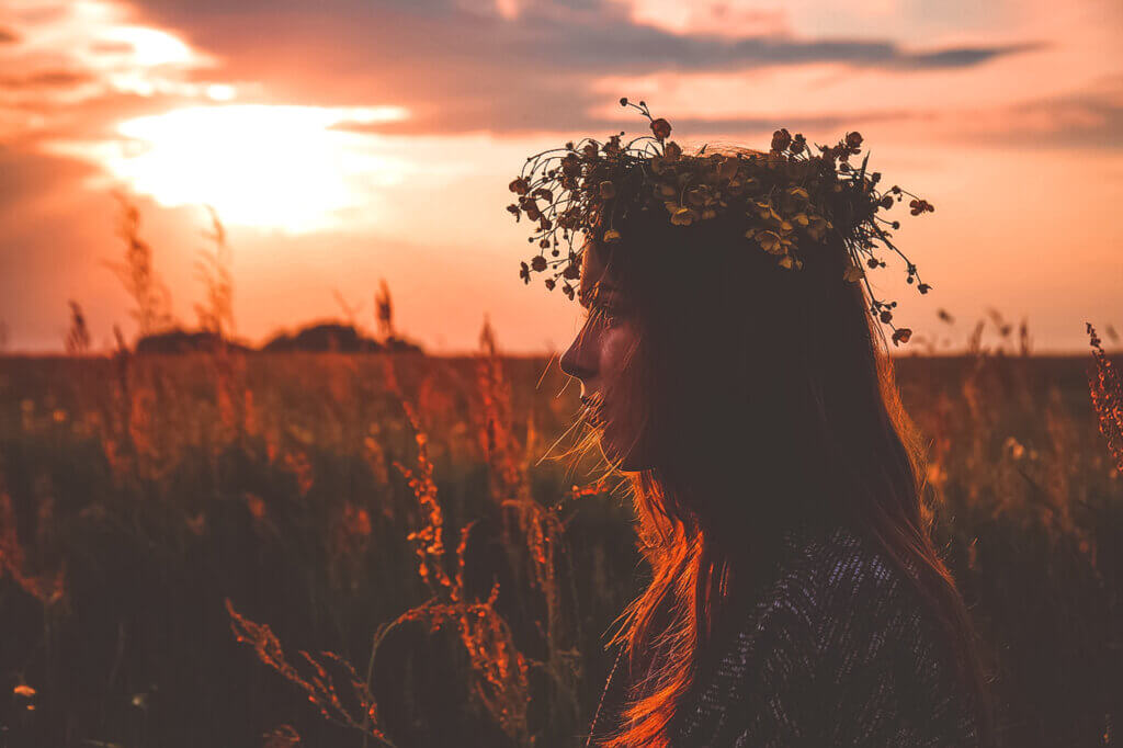 woman sitting in a field at sunset and wearing a crown of wildflowers