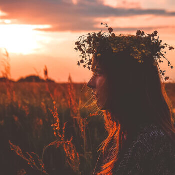 woman sitting in a field at sunset and wearing a crown of wildflowers