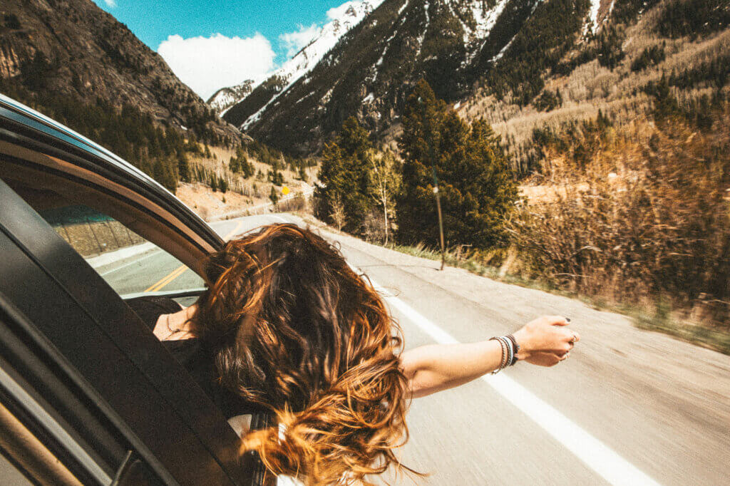 a woman hanging out of a car window in a show of freedom as she's driving through the mountains