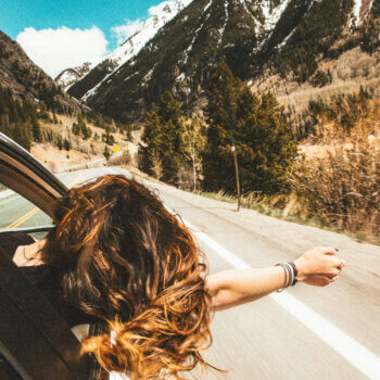 a woman hanging out of a car window in a show of freedom as she's driving through the mountains