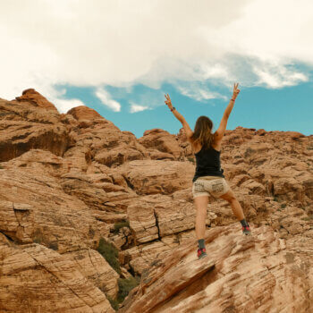 A woman hiking and showing victory with her hands to go with this blog post about overcoming people pleasing and learning to set boundaries