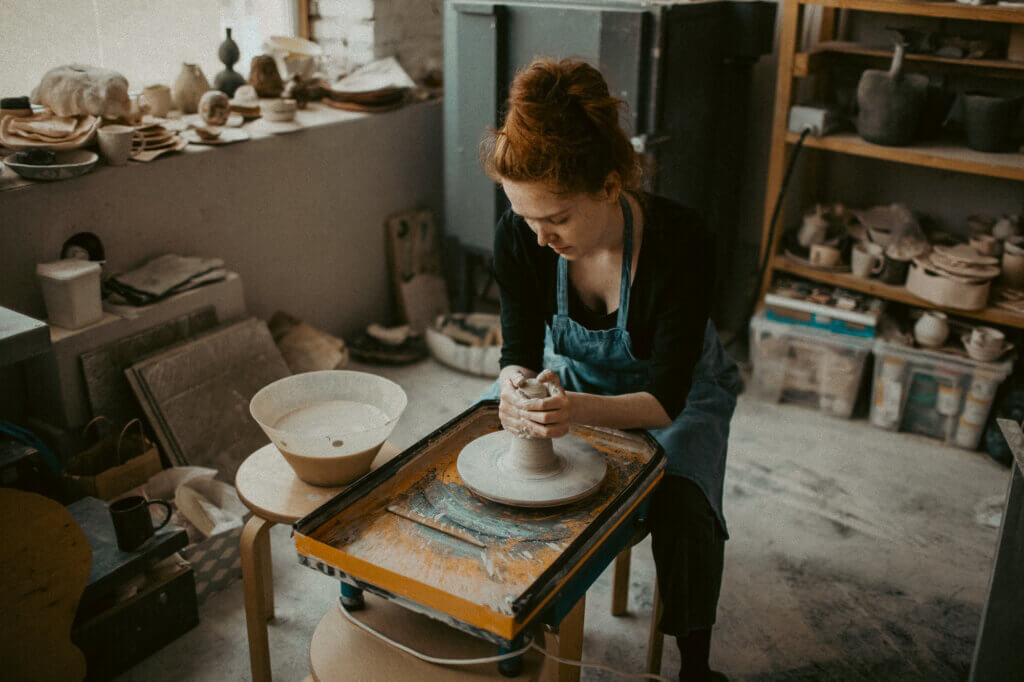 picture of a red-haired woman shaping clay at a potters wheel