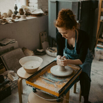 picture of a red-haired woman shaping clay at a potters wheel